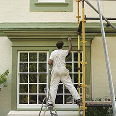 Man on scaffold painting exterior of home
