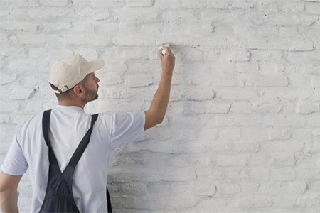 A contractor painting a white brick wall