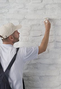 a contractor painting a white brick wall