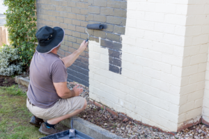 a man painting the brick exterior of his home